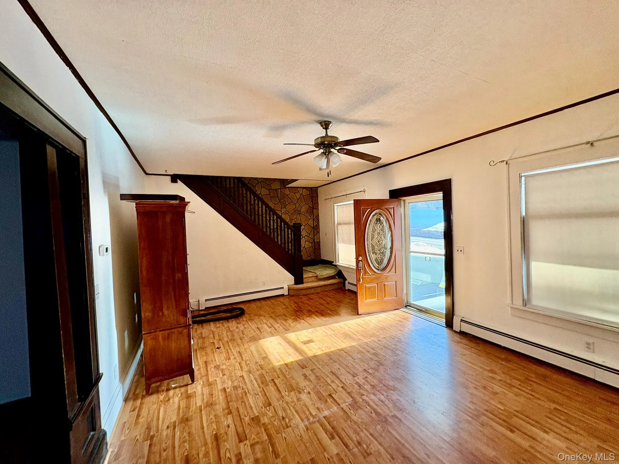 Entryway with light wood-style flooring, a textured ceiling, a baseboard radiator, ceiling fan, and stairs Entryway with light wood-style flooring, a textured ceiling, a baseboard radiator, ceiling fan, and stairs