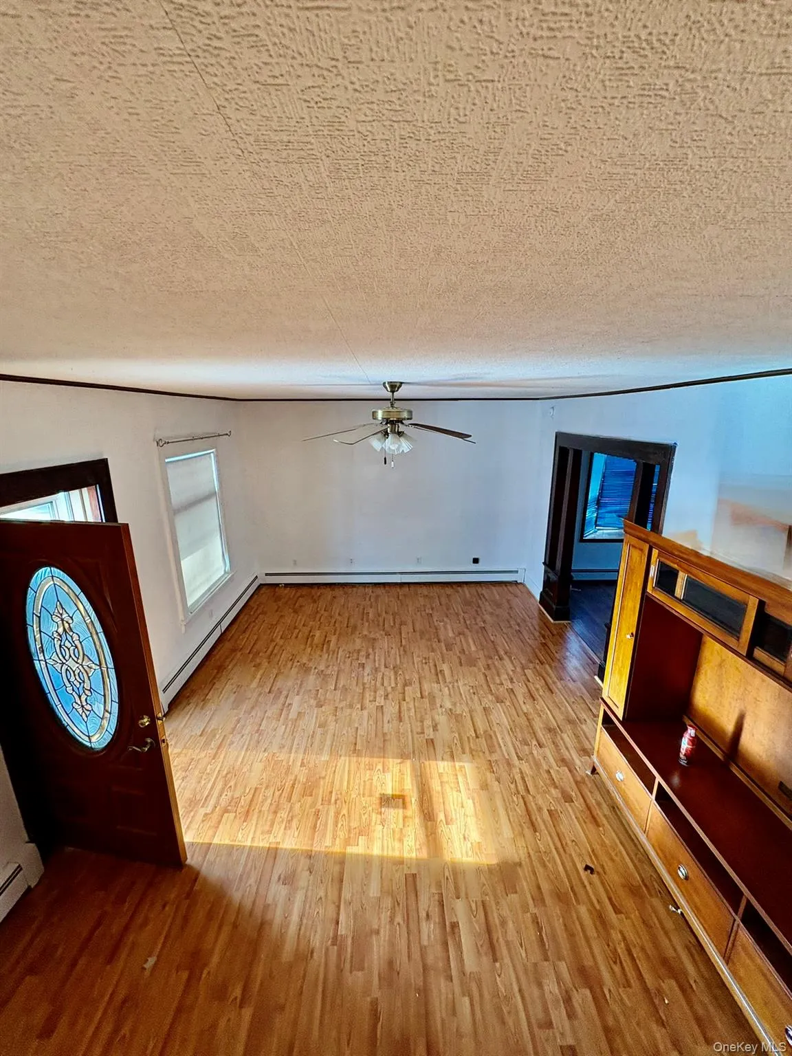 Unfurnished living room featuring wood finished floors, baseboard heating, a ceiling fan, and a textured ceiling Unfurnished living room featuring wood finished floors, baseboard heating, a ceiling fan, and a textured ceiling