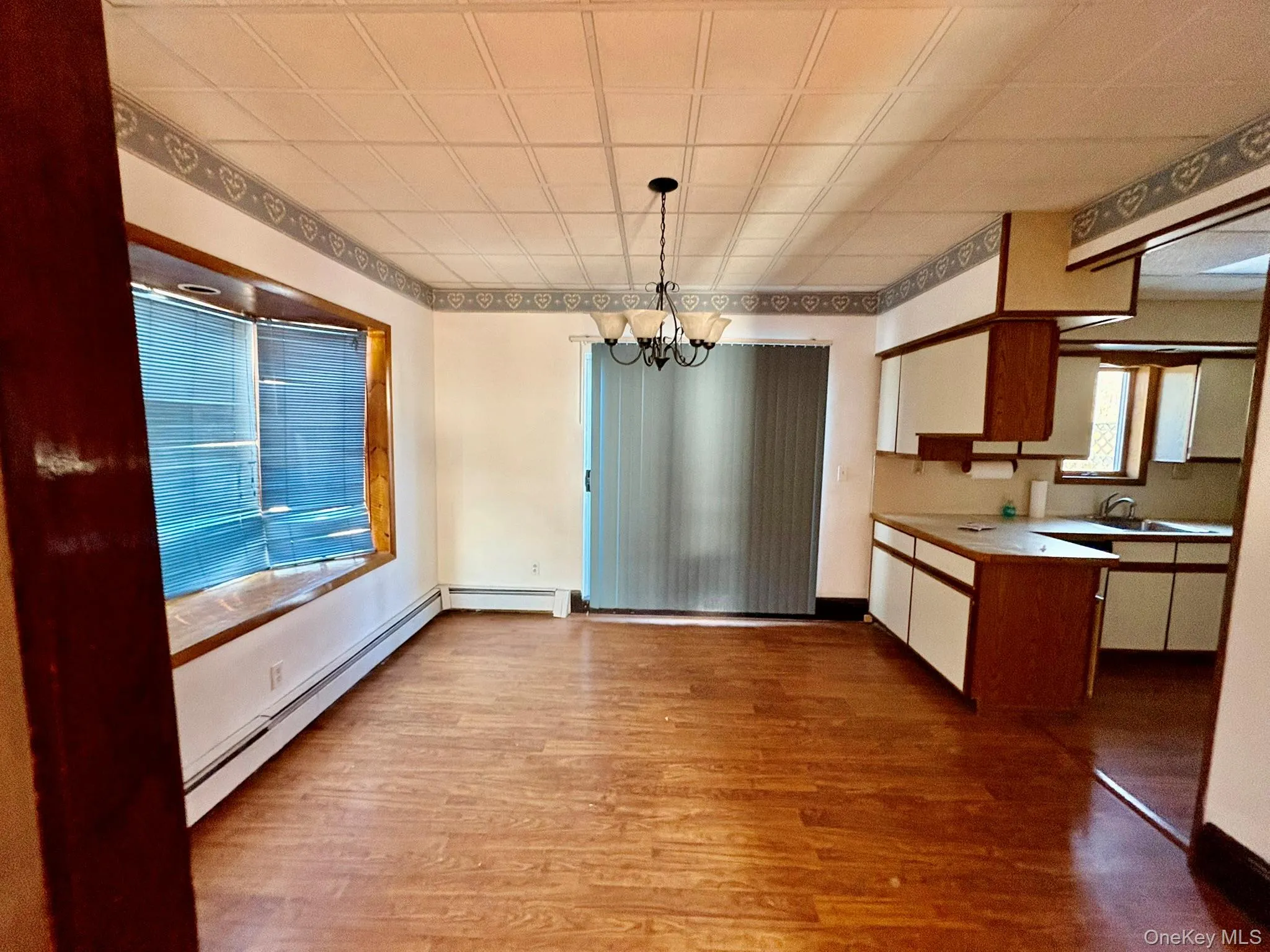 Kitchen with light countertops, a chandelier, brown cabinetry, dark wood finished floors, and baseboard heating Kitchen with light countertops, a chandelier, brown cabinetry, dark wood finished floors, and baseboard heating