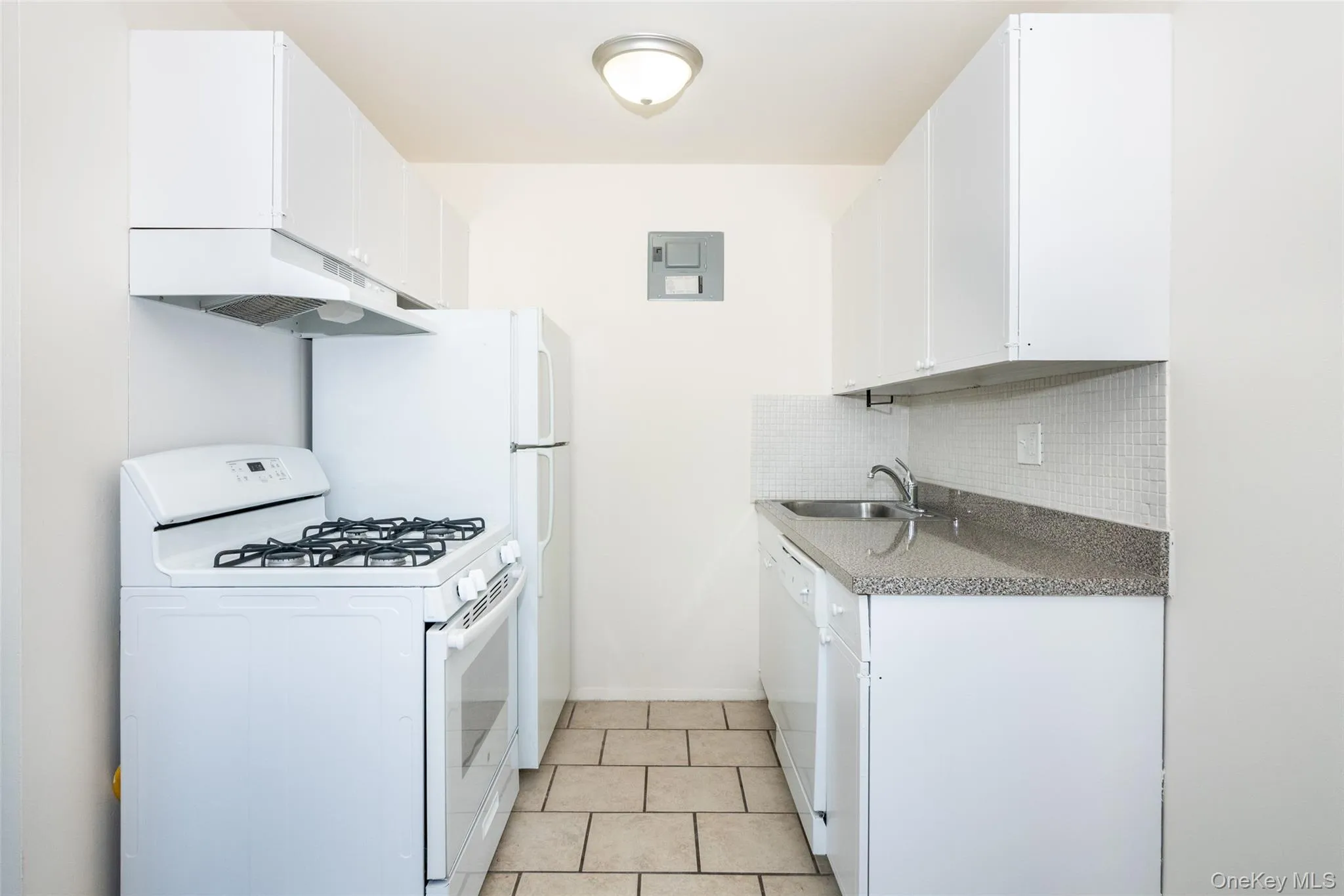 Kitchen featuring white appliances, white cabinetry, under cabinet range hood, backsplash, and light tile patterned flooring Kitchen featuring white appliances, white cabinetry, under cabinet range hood, backsplash, and light tile patterned flooring