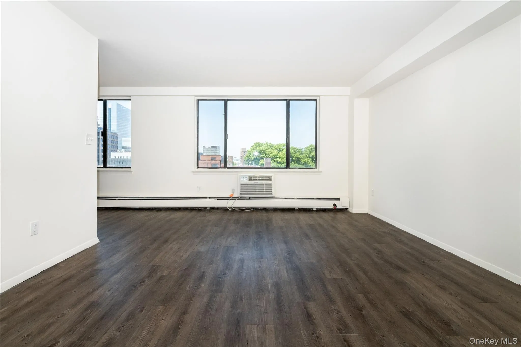 Unfurnished room featuring dark wood finished floors, baseboard heating, and a wall unit AC Unfurnished room featuring dark wood finished floors, baseboard heating, and a wall unit AC