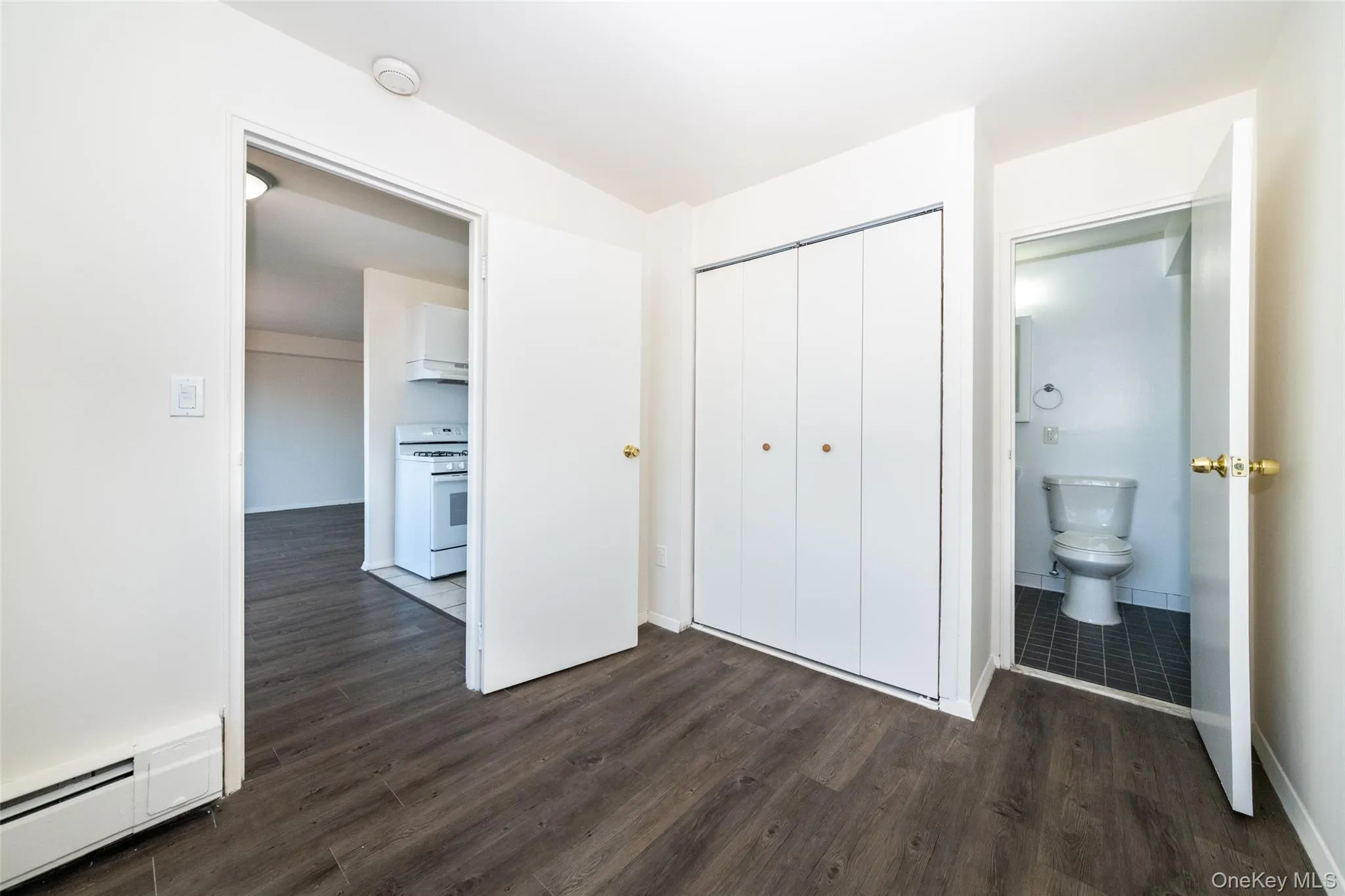 Unfurnished bedroom featuring a baseboard heating unit, dark wood-style floors, and a closet Unfurnished bedroom featuring a baseboard heating unit, dark wood-style floors, and a closet