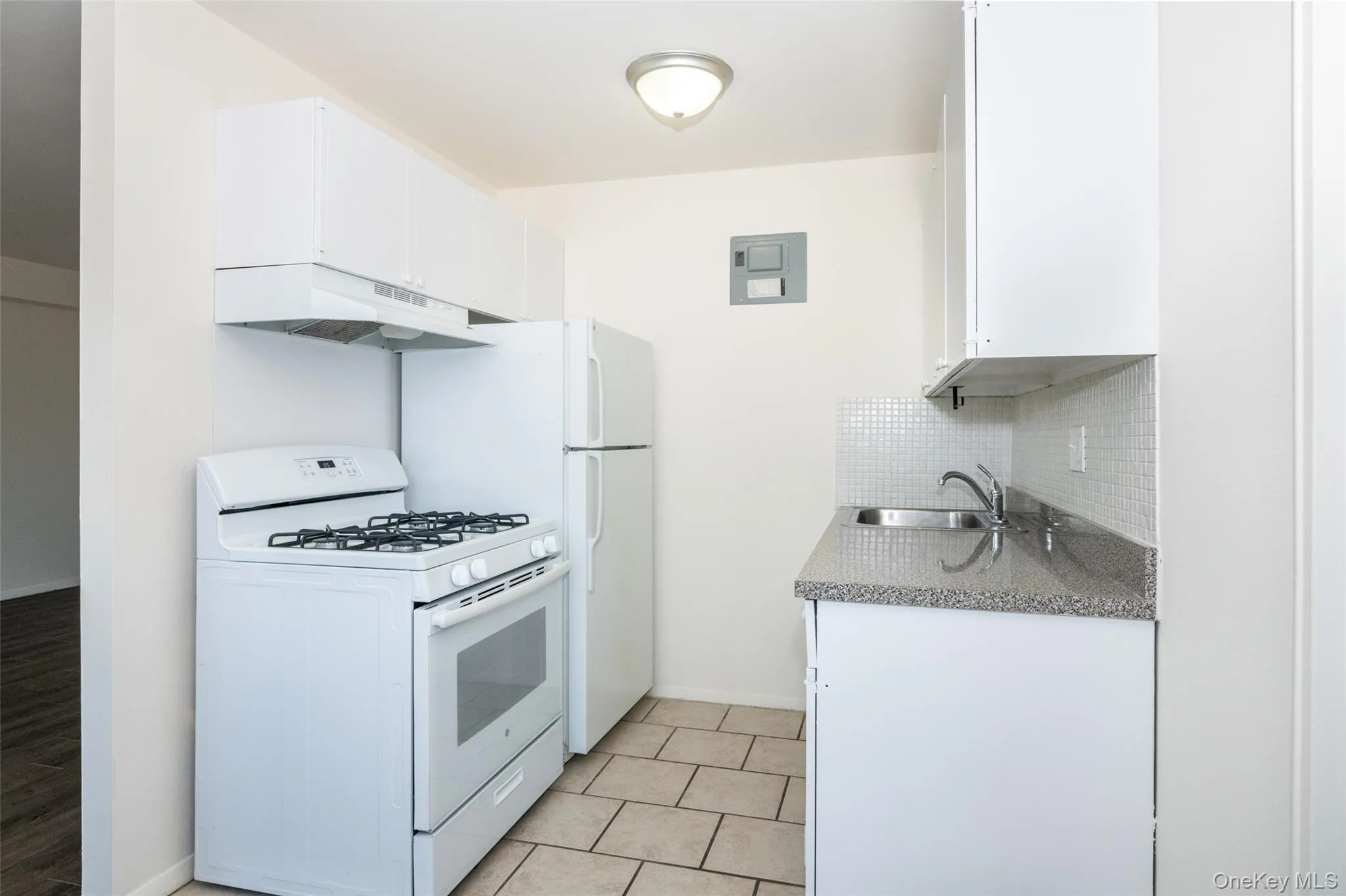 Kitchen with white appliances, white cabinets, under cabinet range hood, and light stone counters Kitchen with white appliances, white cabinets, under cabinet range hood, and light stone counters