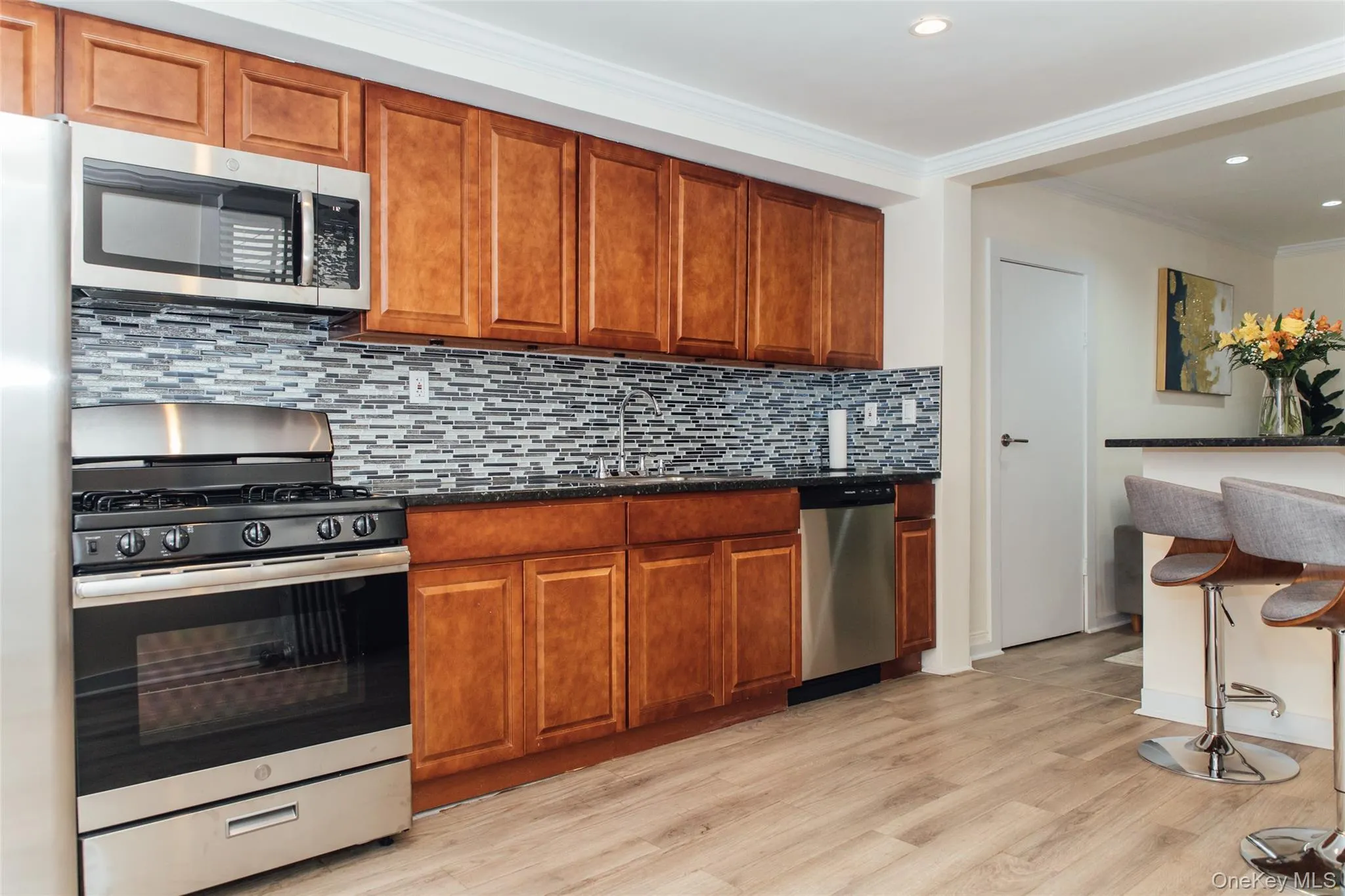 Kitchen with stainless steel appliances, brown cabinets, light wood-style floors, decorative backsplash, and crown molding Kitchen with stainless steel appliances, brown cabinets, light wood-style floors, decorative backsplash, and crown molding