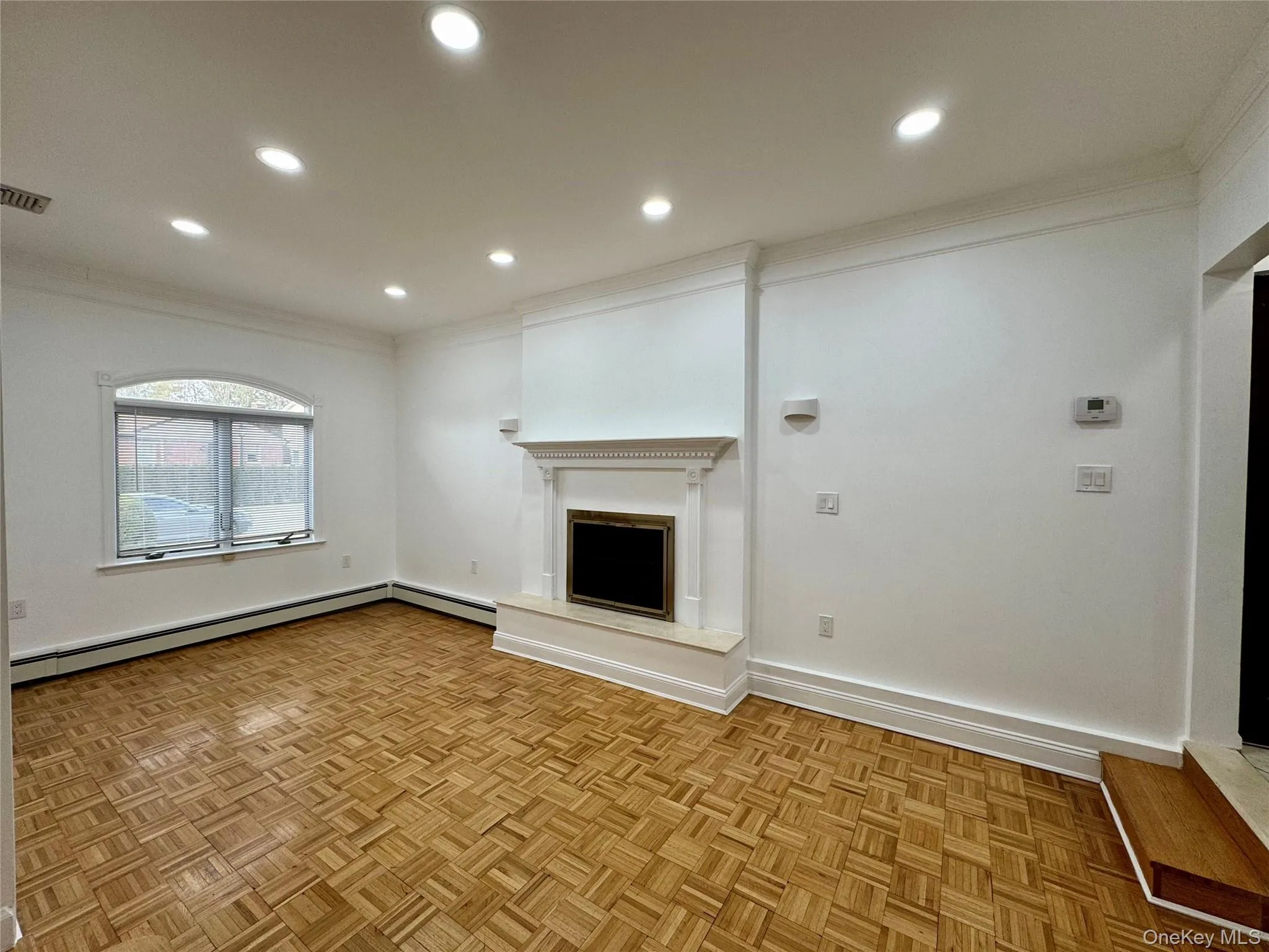 Unfurnished living room with crown molding, a fireplace with raised hearth, recessed lighting, and baseboard heating Unfurnished living room with crown molding, a fireplace with raised hearth, recessed lighting, and baseboard heating