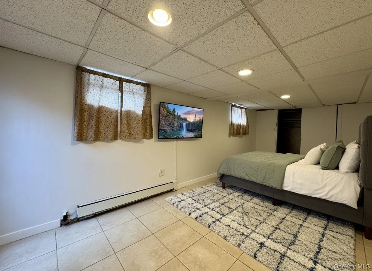 Bedroom featuring a drop ceiling, a baseboard heating unit, and tile patterned floors Bedroom featuring a drop ceiling, a baseboard heating unit, and tile patterned floors