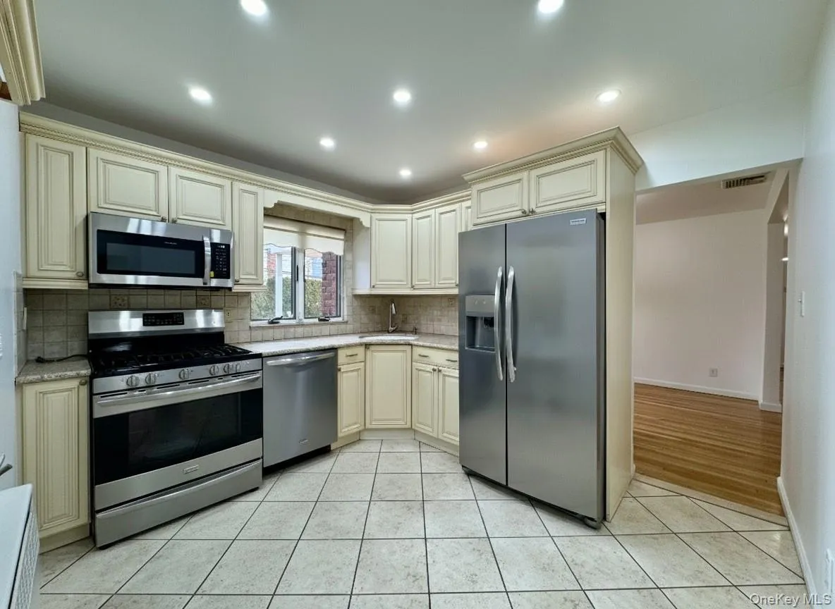 Kitchen with cream cabinetry, stainless steel appliances, light tile patterned floors, recessed lighting, and decorative backsplash Kitchen with cream cabinetry, stainless steel appliances, light tile patterned floors, recessed lighting, and decorative backsplash