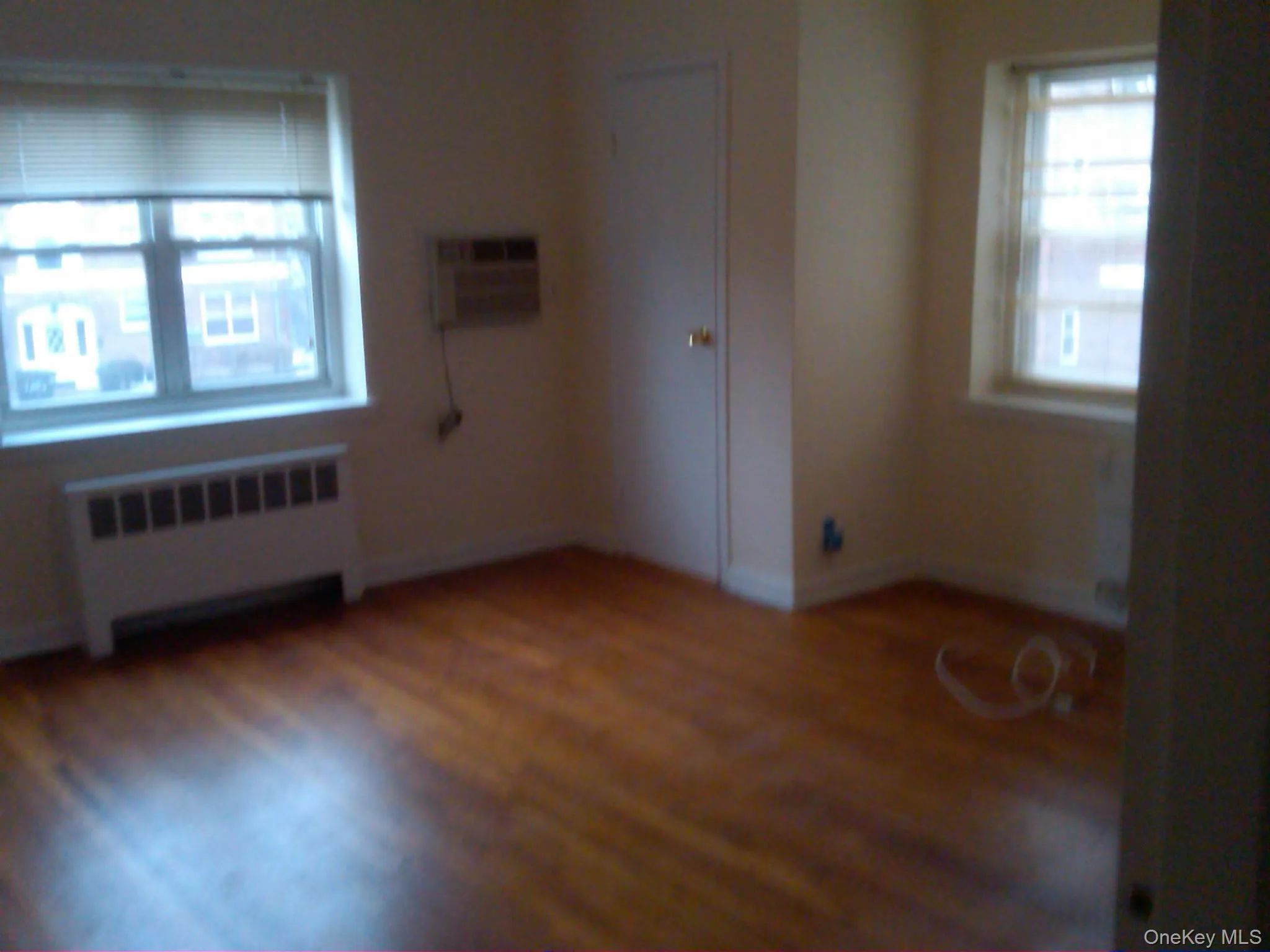 Unfurnished room with radiator heating unit, dark wood-style floors, healthy amount of natural light, and a wall mounted air conditioner Unfurnished room with radiator heating unit, dark wood-style floors, healthy amount of natural light, and a wall mounted air conditioner