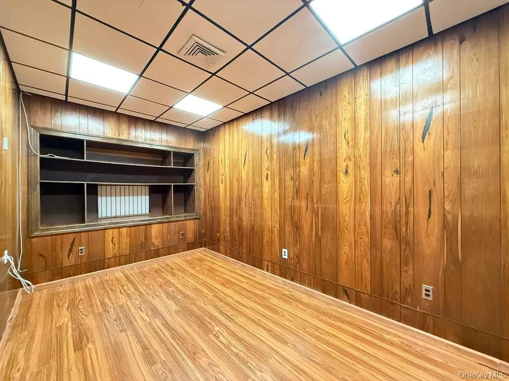 Empty room with built in features, wooden walls, wood finished floors, and a drop ceiling Empty room with built in features, wooden walls, wood finished floors, and a drop ceiling