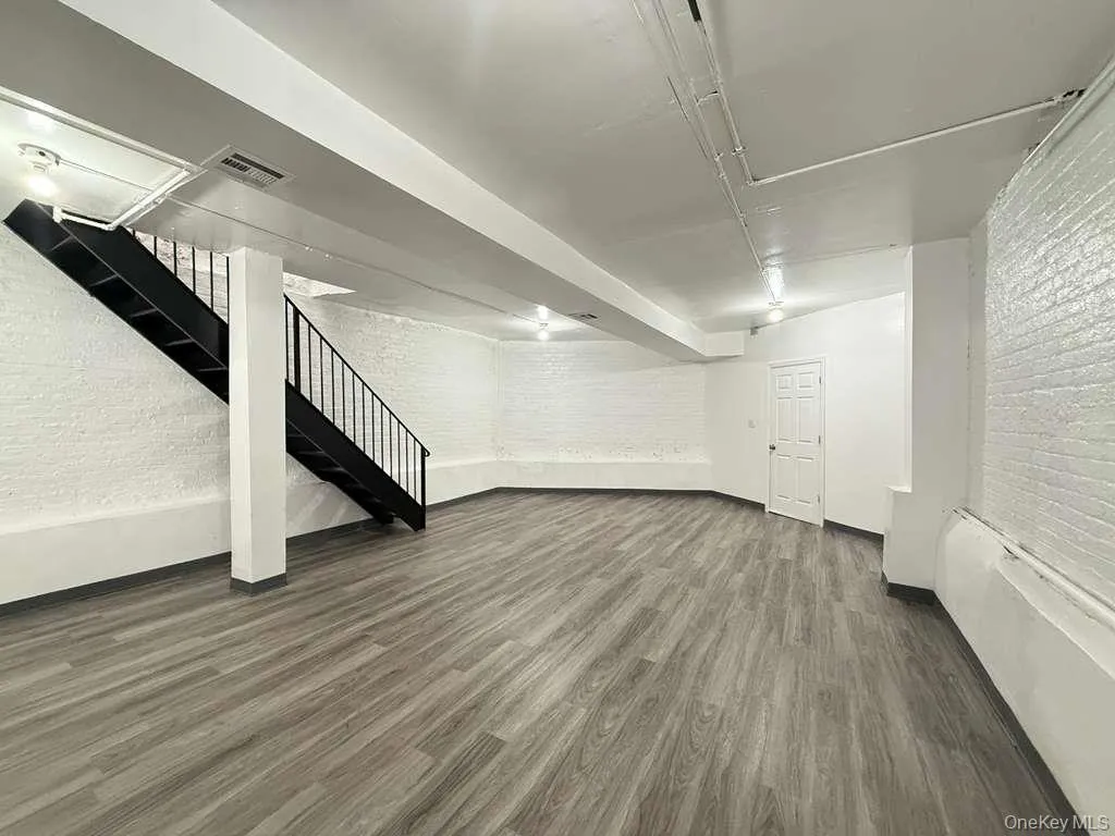 Finished below grade area featuring brick wall, dark wood-style flooring, and stairway Finished below grade area featuring brick wall, dark wood-style flooring, and stairway