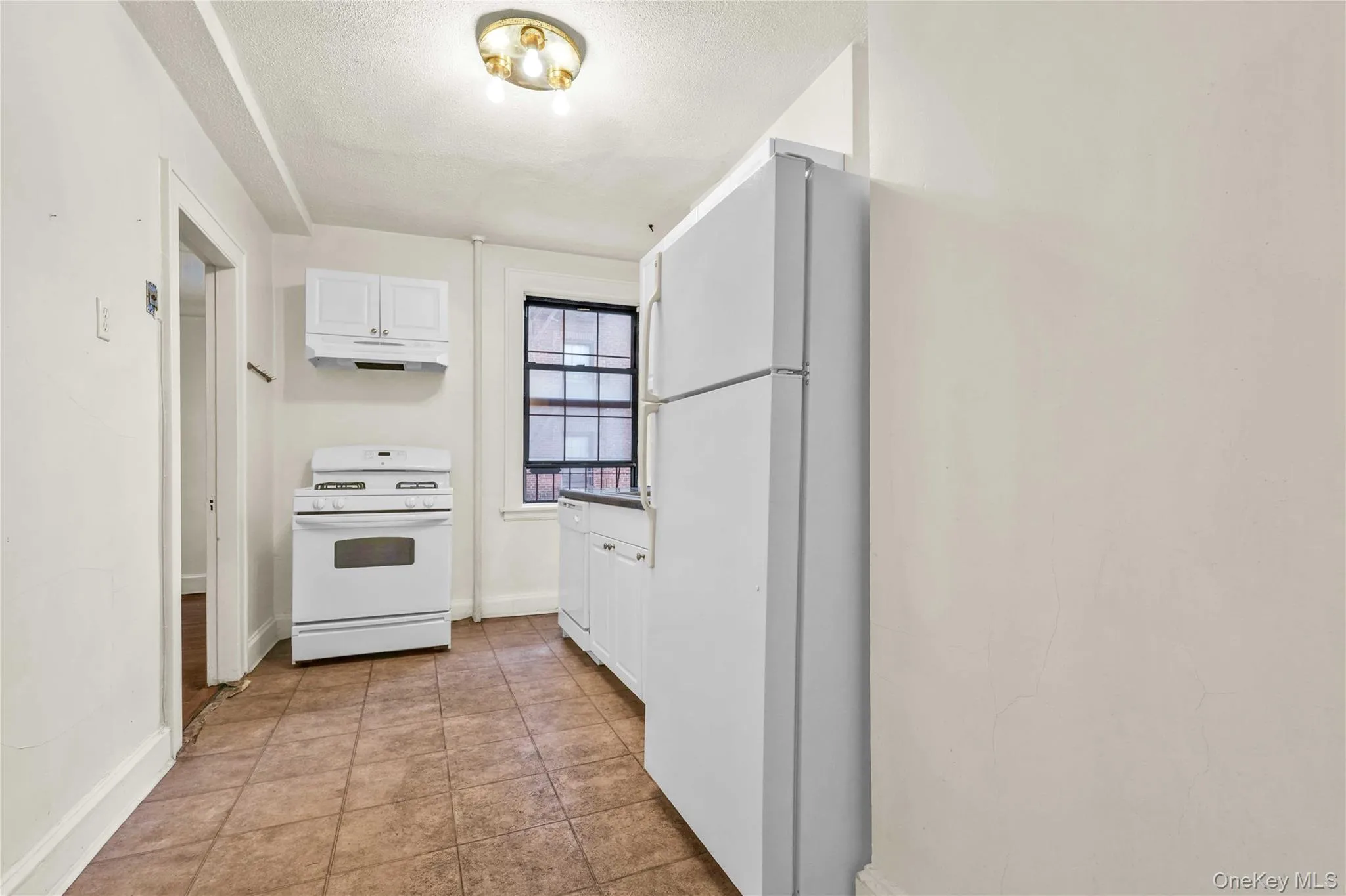Kitchen featuring white appliances, white cabinets, a textured ceiling, under cabinet range hood, and dark tile patterned flooring Kitchen featuring white appliances, white cabinets, a textured ceiling, under cabinet range hood, and dark tile patterned flooring
