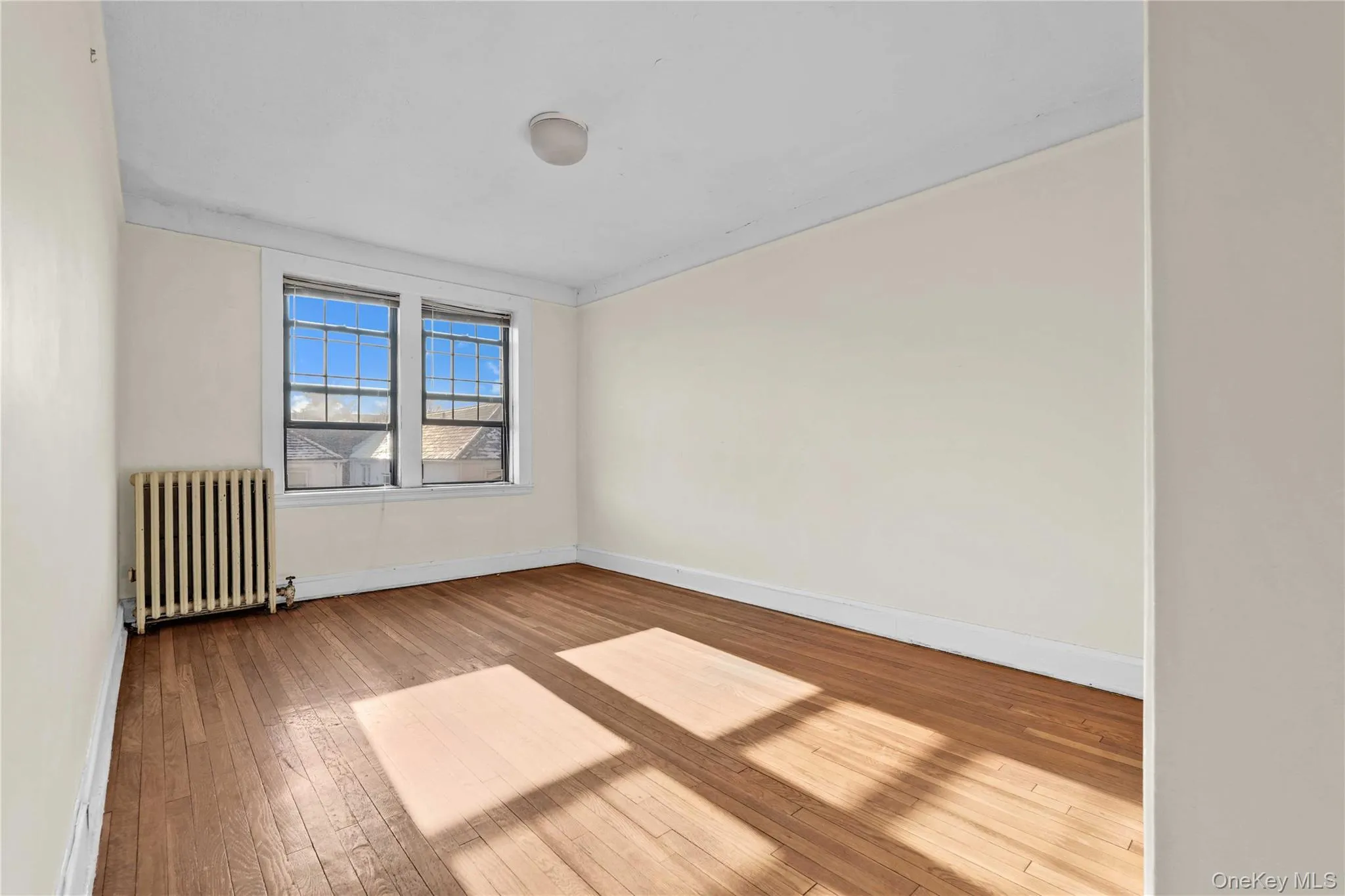 Unfurnished room featuring radiator and light wood-style flooring Unfurnished room featuring radiator and light wood-style flooring
