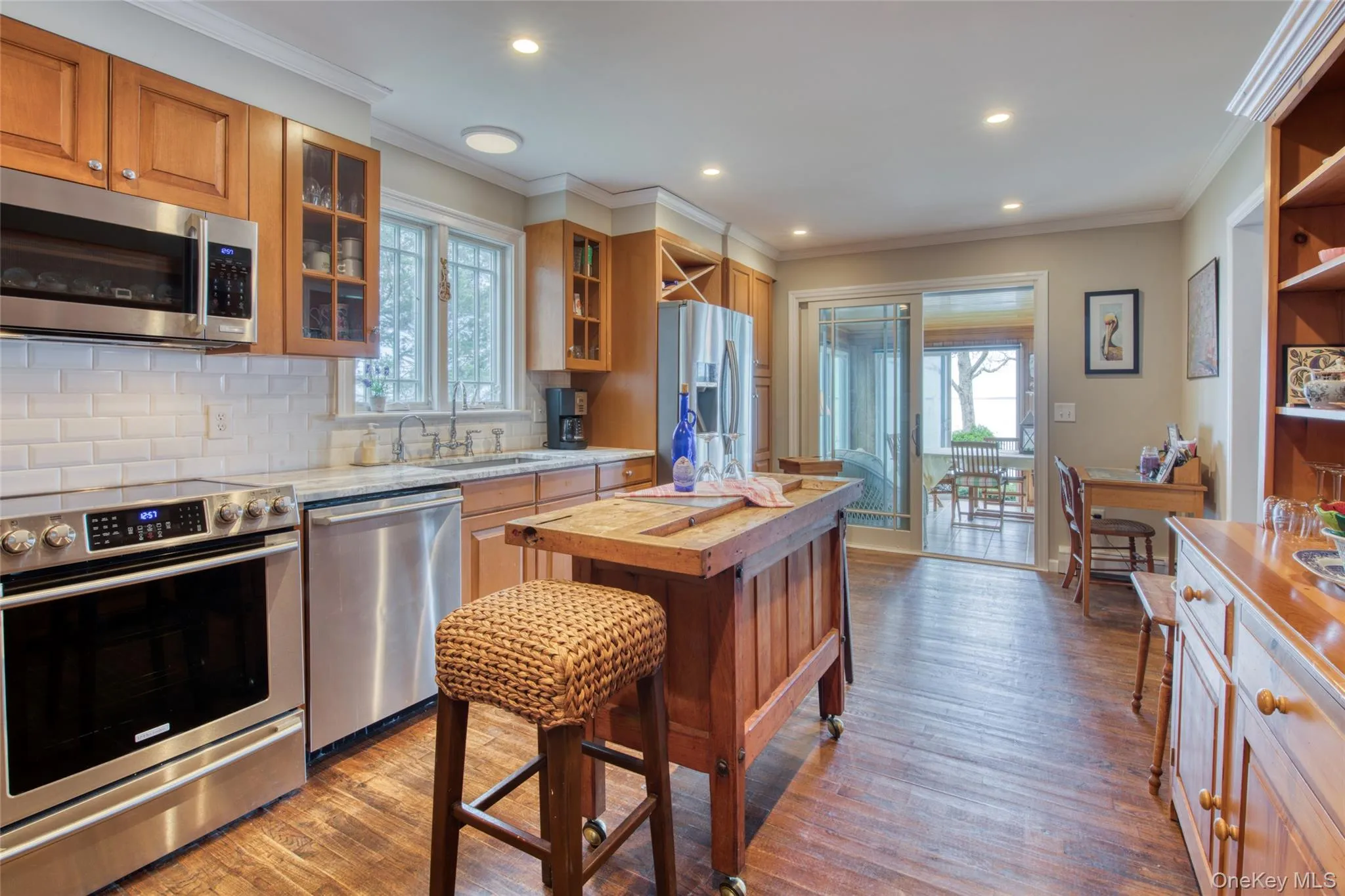 Kitchen with appliances with stainless steel finishes, dark wood-style flooring, crown molding, glass insert cabinets, and backsplash. center island for add'l food preparation Kitchen with appliances with stainless steel finishes, dark wood-style flooring, crown molding, glass insert cabinets, and backsplash. center island for add'l food preparation
