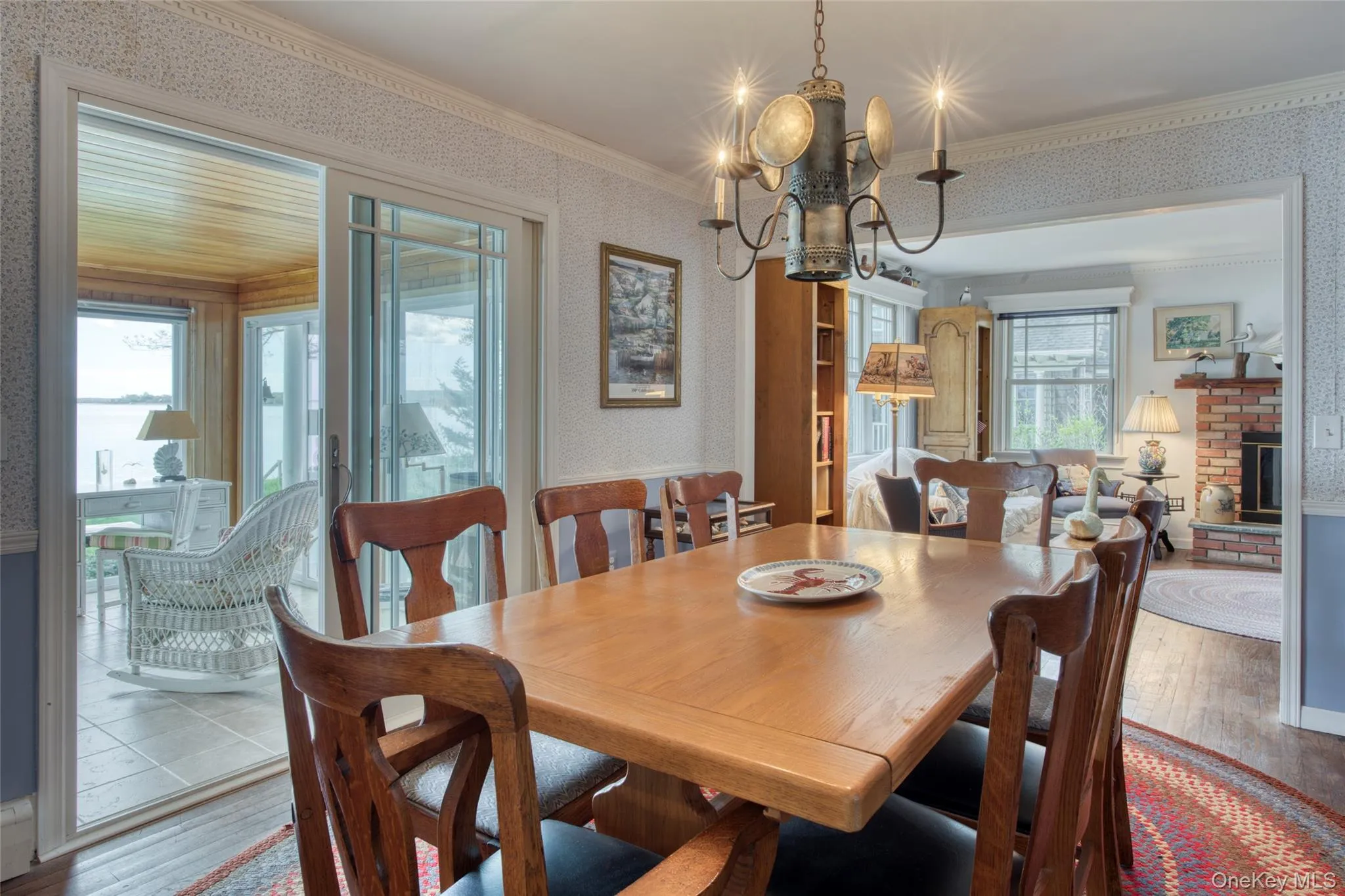 Dining room featuring wallpapered walls, hardwood / wood-style flooring, ornamental molding, a chandelier, and a brick fireplace Dining room featuring wallpapered walls, hardwood / wood-style flooring, ornamental molding, a chandelier, and a brick fireplace