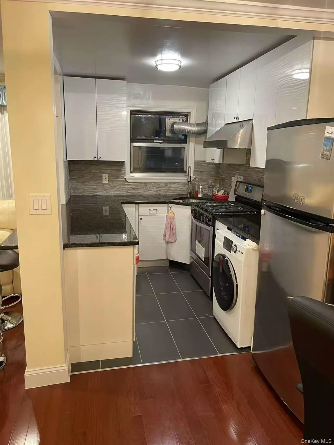 Kitchen with stainless steel appliances, decorative backsplash, washer / clothes dryer, dark stone countertops, and under cabinet range hood Kitchen with stainless steel appliances, decorative backsplash, washer / clothes dryer, dark stone countertops, and under cabinet range hood