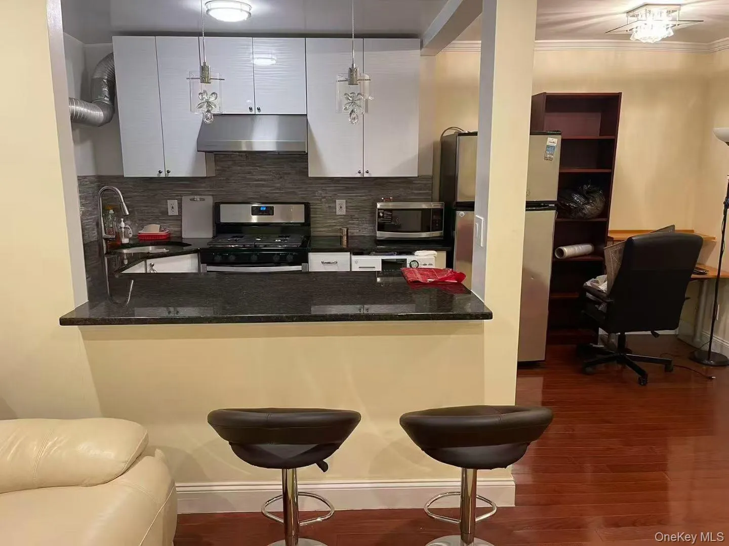 Kitchen featuring a kitchen breakfast bar, backsplash, stainless steel appliances, a peninsula, and under cabinet range hood Kitchen featuring a kitchen breakfast bar, backsplash, stainless steel appliances, a peninsula, and under cabinet range hood