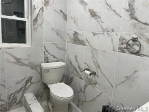 Full bathroom featuring marble finish flooring, tile walls, and a marble finish shower Full bathroom featuring marble finish flooring, tile walls, and a marble finish shower