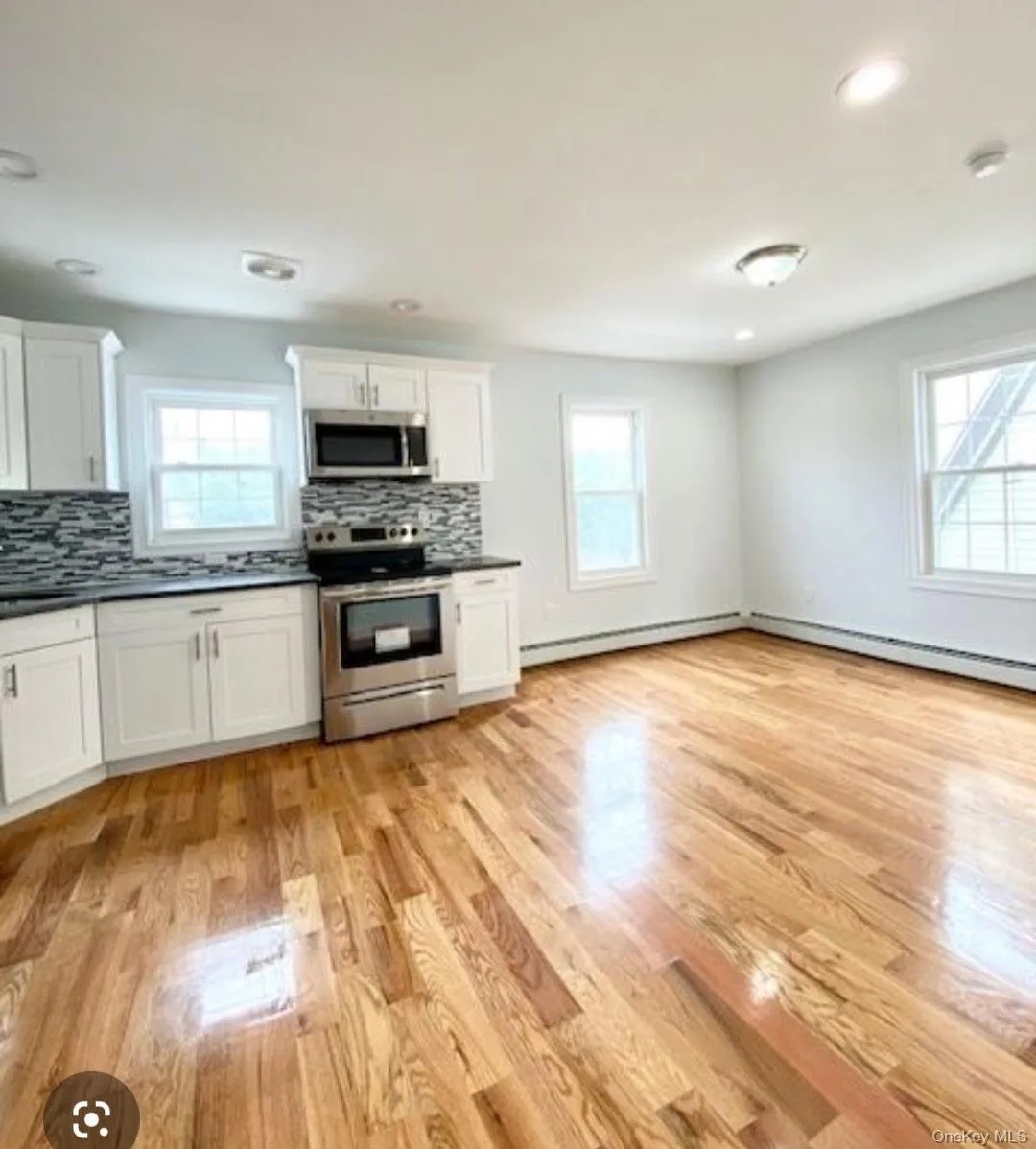 Kitchen with dark countertops, appliances with stainless steel finishes, white cabinets, backsplash, and light wood-type flooring Kitchen with dark countertops, appliances with stainless steel finishes, white cabinets, backsplash, and light wood-type flooring