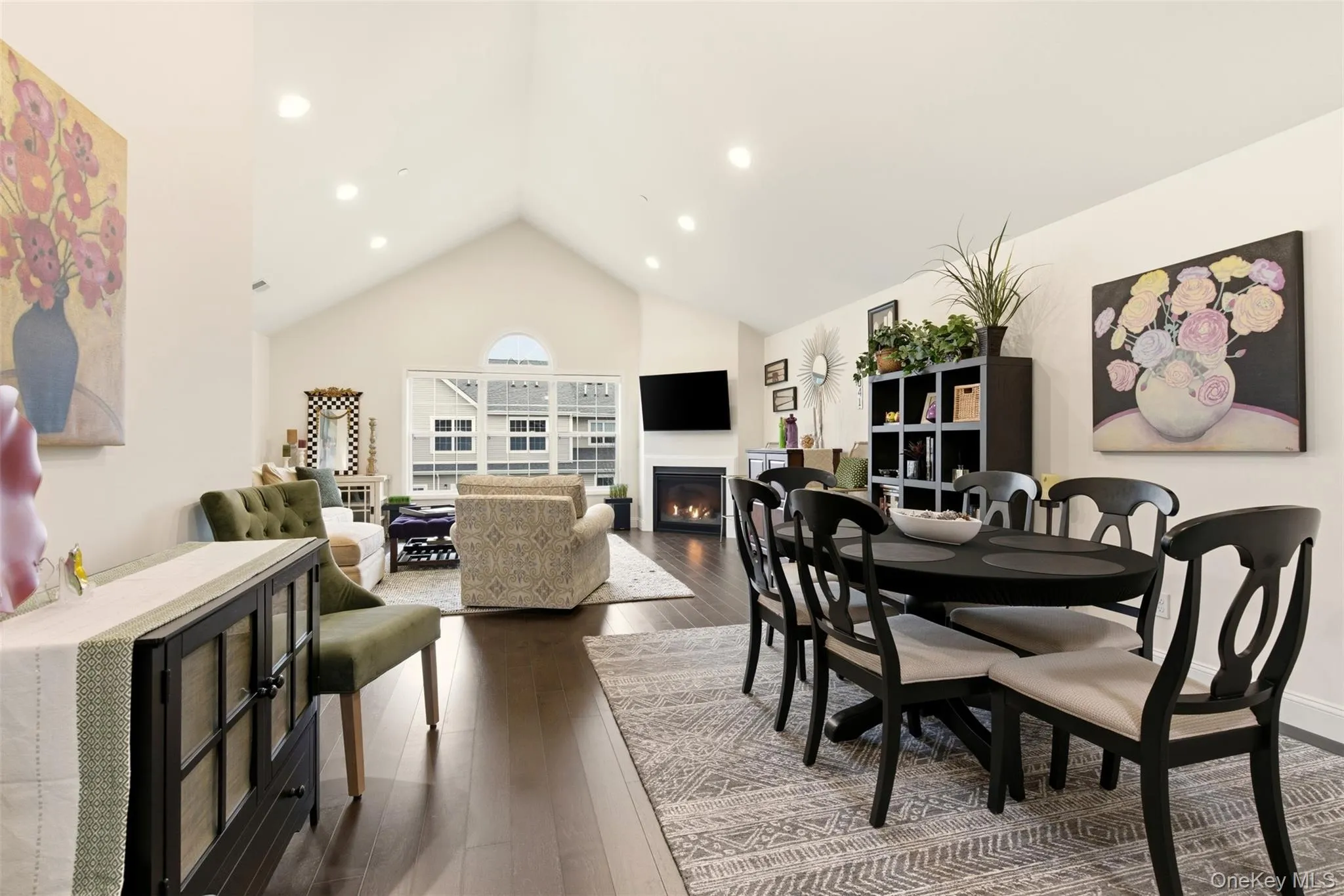 Dining space with a lit fireplace, dark wood finished floors, and high vaulted ceiling Dining space with a lit fireplace, dark wood finished floors, and high vaulted ceiling