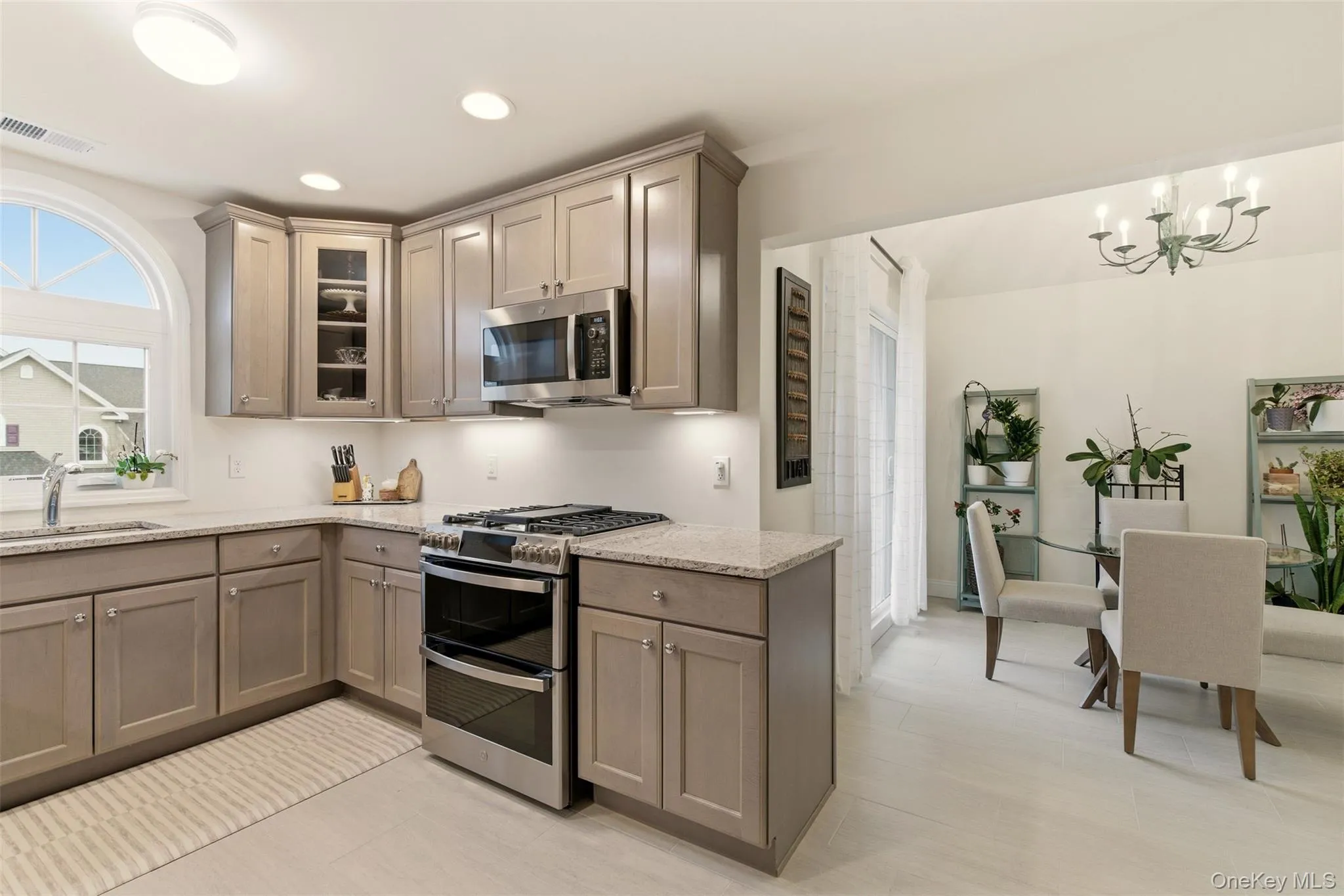 Kitchen featuring appliances with stainless steel finishes, light stone countertops, glass insert cabinets, a chandelier, and recessed lighting Kitchen featuring appliances with stainless steel finishes, light stone countertops, glass insert cabinets, a chandelier, and recessed lighting