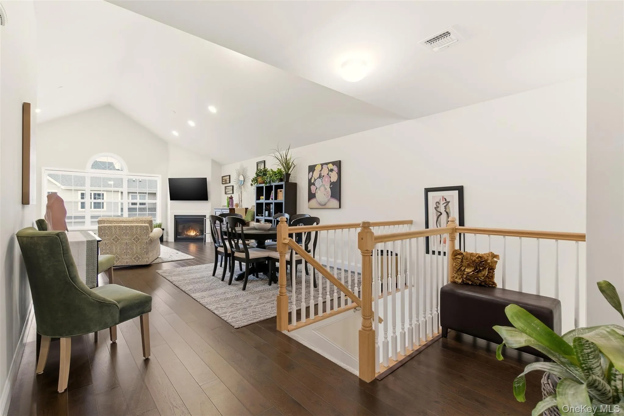 Living area featuring a lit fireplace, dark wood-style flooring, an upstairs landing, and high vaulted ceiling Living area featuring a lit fireplace, dark wood-style flooring, an upstairs landing, and high vaulted ceiling
