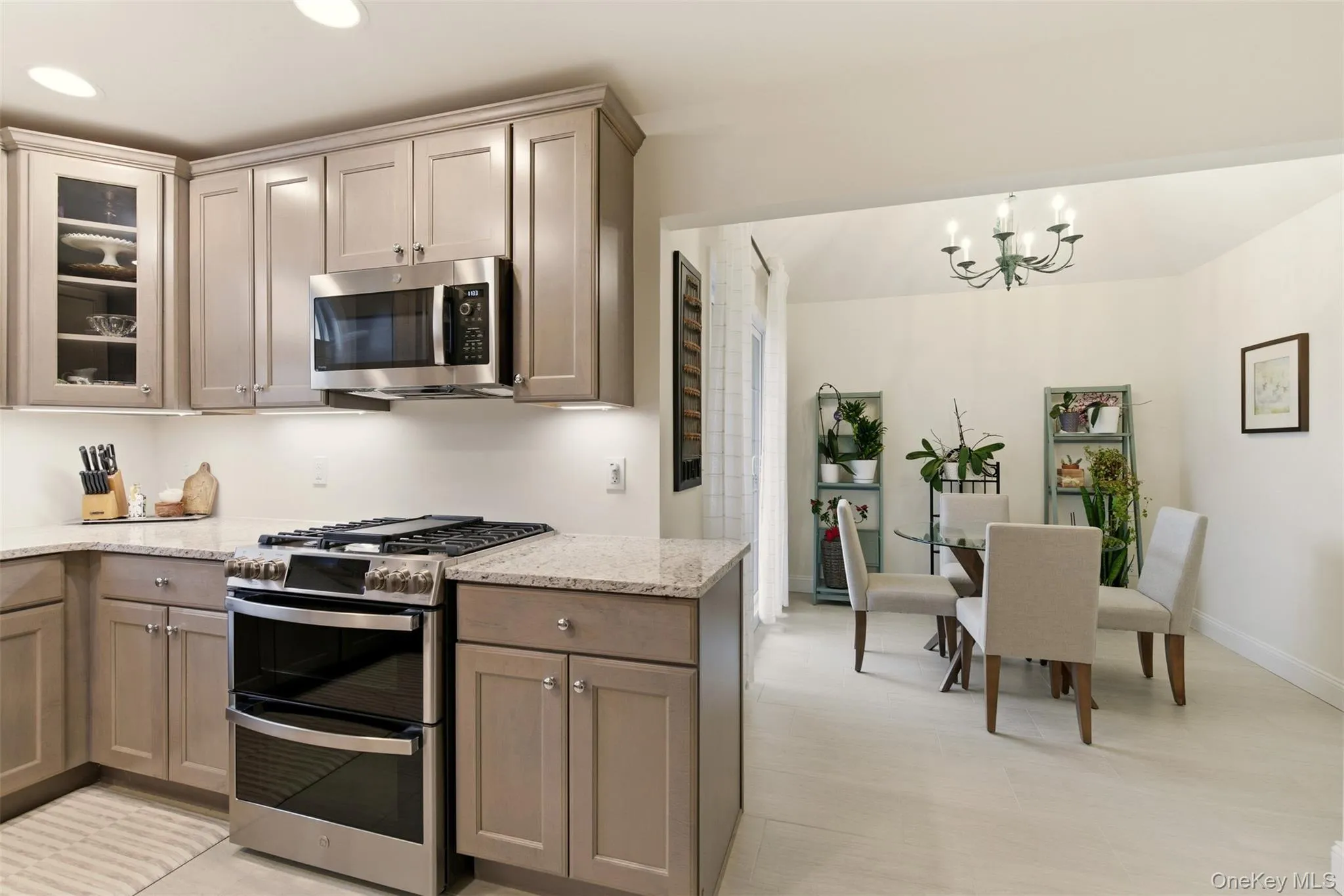 Kitchen with appliances with stainless steel finishes, glass insert cabinets, light stone counters, a chandelier, and hanging light fixtures Kitchen with appliances with stainless steel finishes, glass insert cabinets, light stone counters, a chandelier, and hanging light fixtures