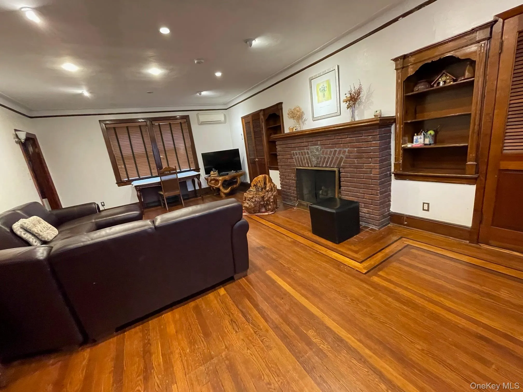 Living area with wood finished floors, a brick fireplace, recessed lighting, ornamental molding, and built in features Living area with wood finished floors, a brick fireplace, recessed lighting, ornamental molding, and built in features