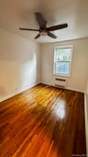Spare room with light wood finished floors, radiator, and a ceiling fan Spare room with light wood finished floors, radiator, and a ceiling fan