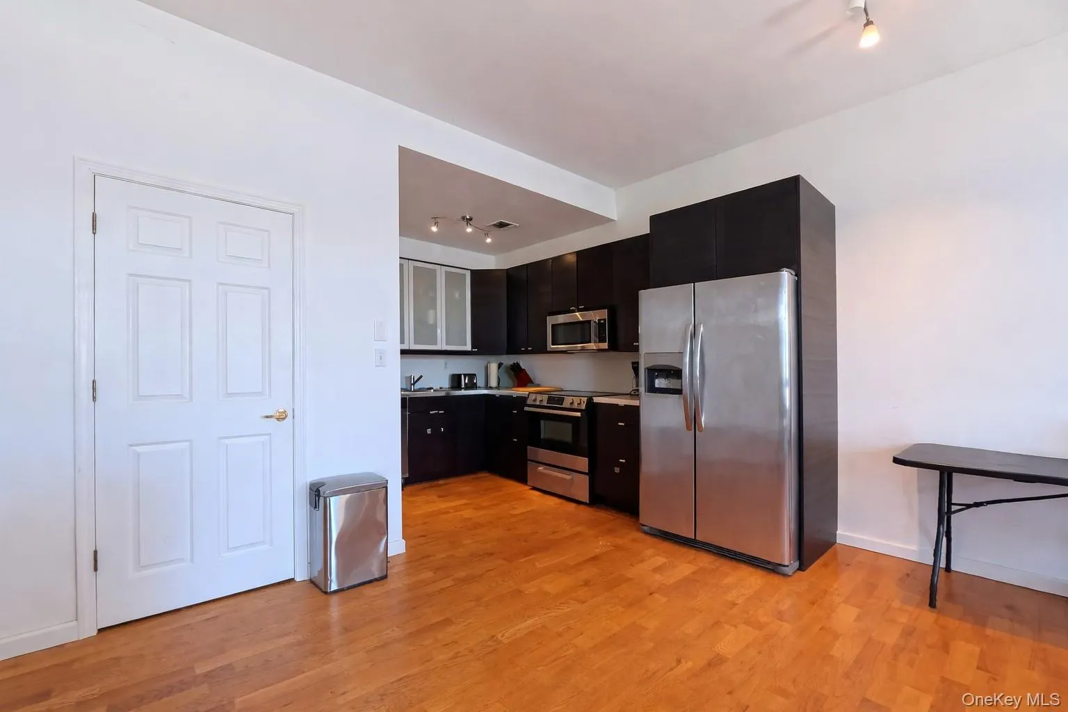 Kitchen with stainless steel appliances, dark cabinets, glass insert cabinets, and rail lighting Kitchen with stainless steel appliances, dark cabinets, glass insert cabinets, and rail lighting