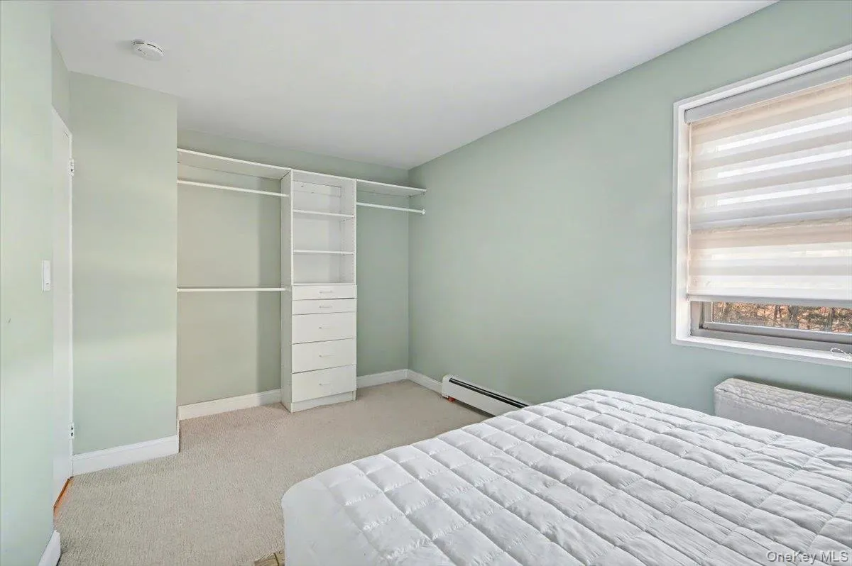 Bedroom with light carpet, a baseboard heating unit, and a opencloset Bedroom with light carpet, a baseboard heating unit, and a opencloset