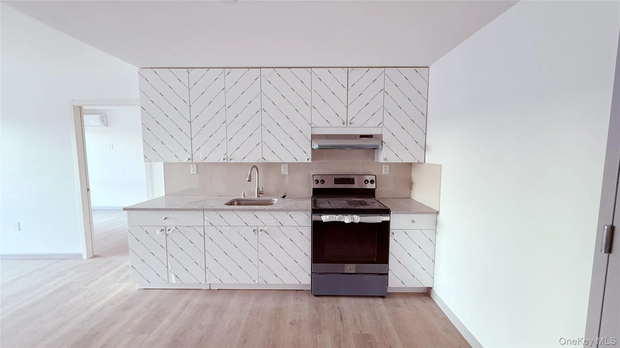 Kitchen with electric range, white cabinetry, decorative backsplash, and light wood-type flooring Kitchen with electric range, white cabinetry, decorative backsplash, and light wood-type flooring