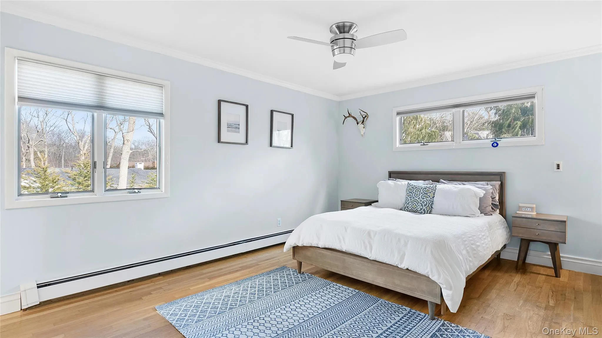 Bedroom with baseboard heating, ornamental molding, light wood-style flooring, and a ceiling fan Bedroom with baseboard heating, ornamental molding, light wood-style flooring, and a ceiling fan