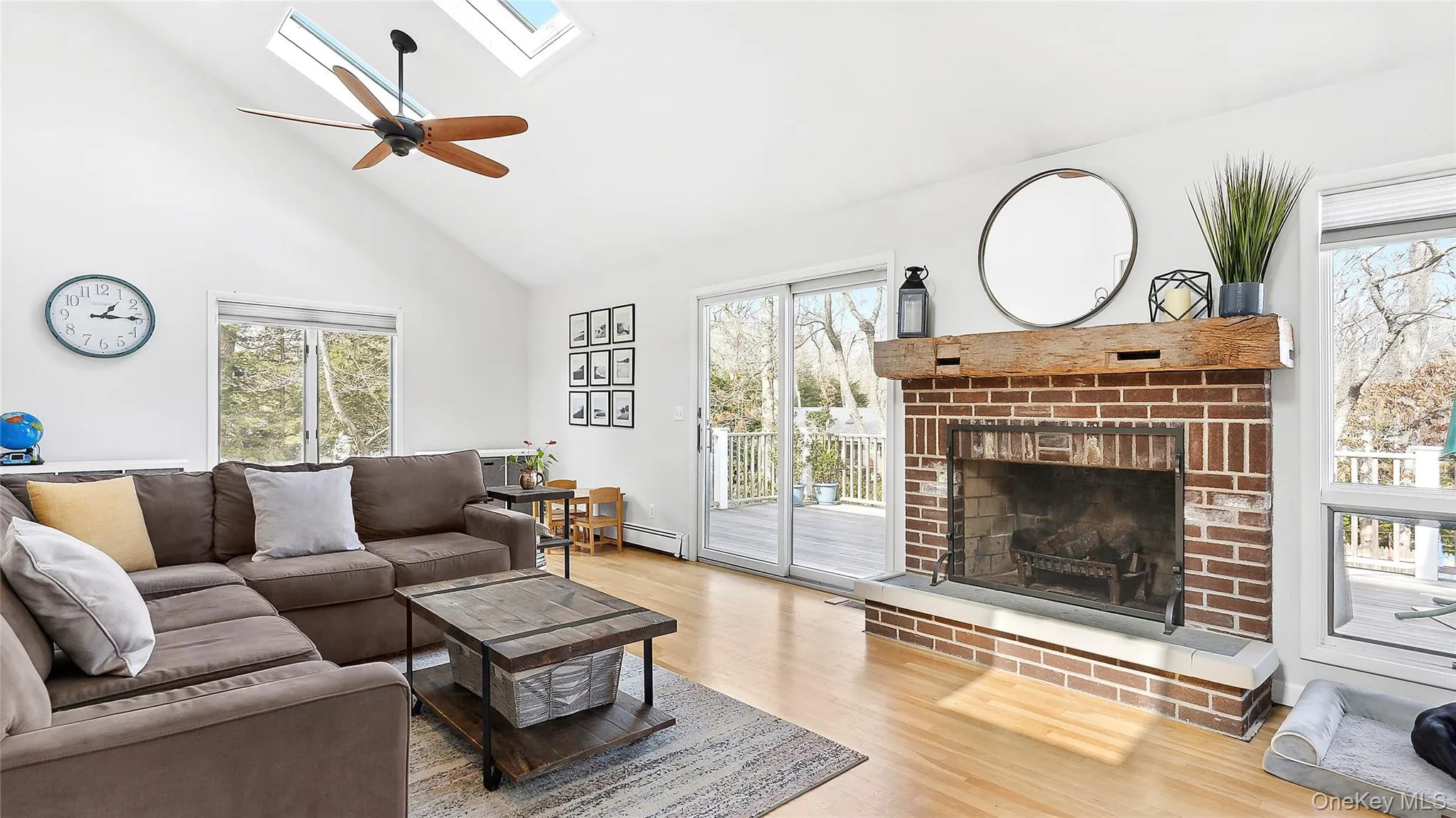 Living room featuring a skylight, high vaulted ceiling, wood finished floors, healthy amount of natural light, and a brick fireplace Living room featuring a skylight, high vaulted ceiling, wood finished floors, healthy amount of natural light, and a brick fireplace