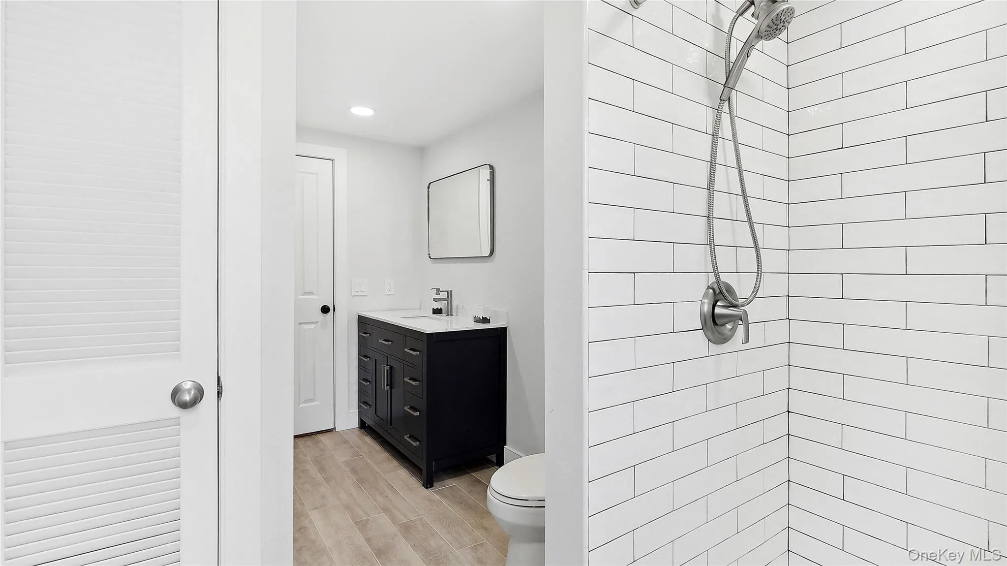Full bathroom featuring vanity, a tile shower, wood finish floors, and recessed lighting Full bathroom featuring vanity, a tile shower, wood finish floors, and recessed lighting