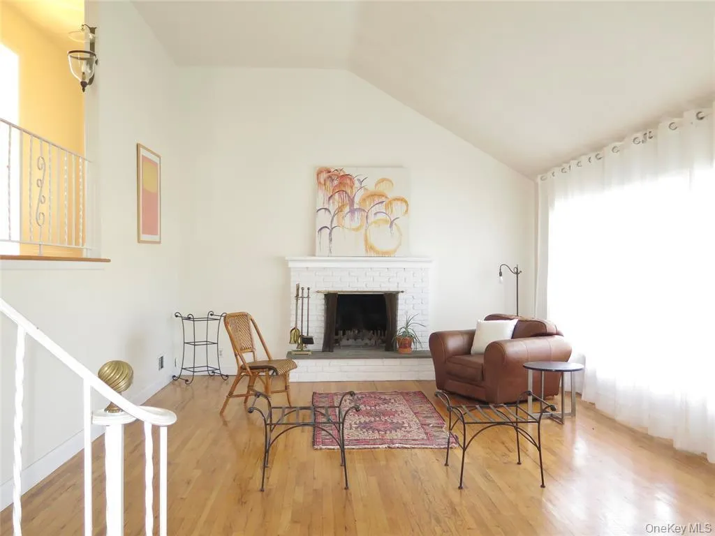 Living area with healthy amount of natural light, vaulted ceiling, a brick fireplace, and wood finished floors Living area with healthy amount of natural light, vaulted ceiling, a brick fireplace, and wood finished floors