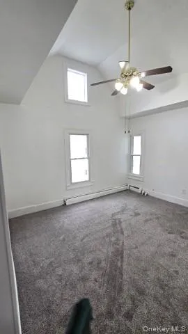 Unfurnished room featuring dark colored carpet, a baseboard heating unit, and high vaulted ceiling Unfurnished room featuring dark colored carpet, a baseboard heating unit, and high vaulted ceiling