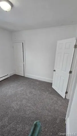 Spare room featuring dark colored carpet and a baseboard heating unit Spare room featuring dark colored carpet and a baseboard heating unit
