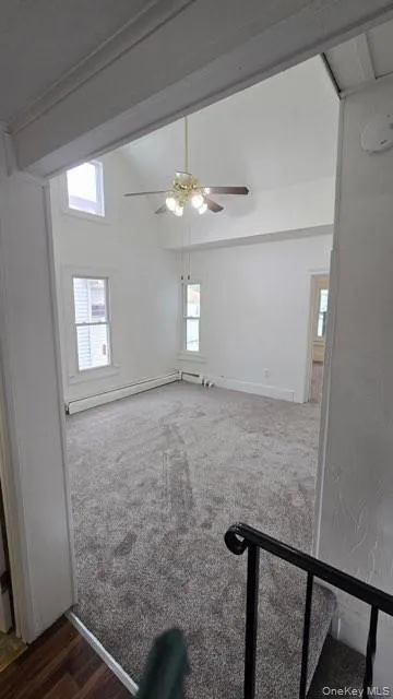 Unfurnished room with dark carpet, baseboard heating, and a ceiling fan Unfurnished room with dark carpet, baseboard heating, and a ceiling fan