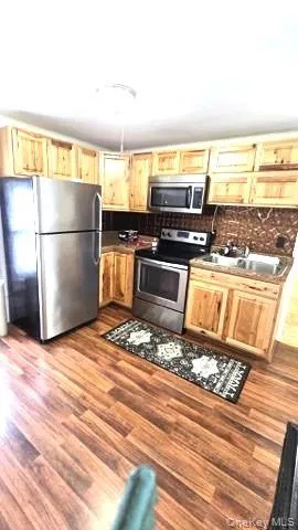 Kitchen with appliances with stainless steel finishes, dark wood-style floors, and light brown cabinetry Kitchen with appliances with stainless steel finishes, dark wood-style floors, and light brown cabinetry
