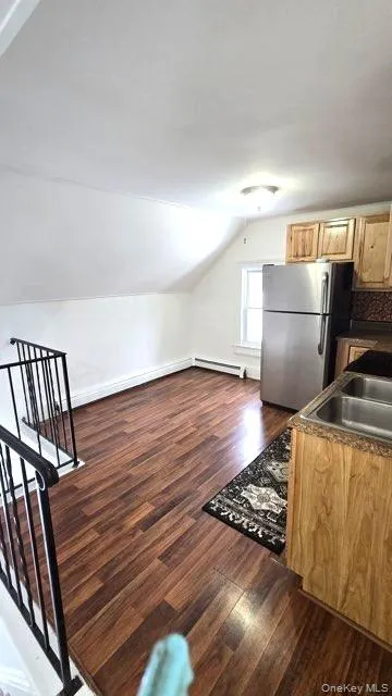 Kitchen featuring freestanding refrigerator, dark wood finished floors, vaulted ceiling, and dark countertops Kitchen featuring freestanding refrigerator, dark wood finished floors, vaulted ceiling, and dark countertops