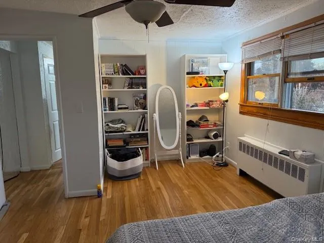 Bedroom featuring radiator heating unit, a textured ceiling, light wood-style floors, and ceiling fan Bedroom featuring radiator heating unit, a textured ceiling, light wood-style floors, and ceiling fan
