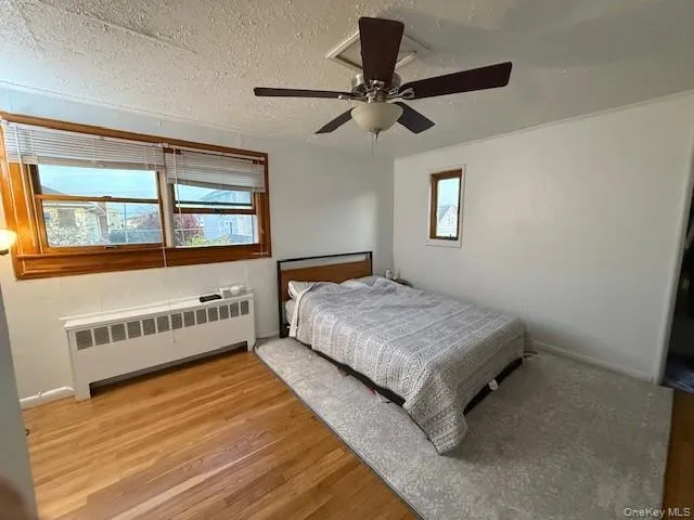 Bedroom featuring radiator heating unit, light wood-style floors, a ceiling fan, and a textured ceiling Bedroom featuring radiator heating unit, light wood-style floors, a ceiling fan, and a textured ceiling