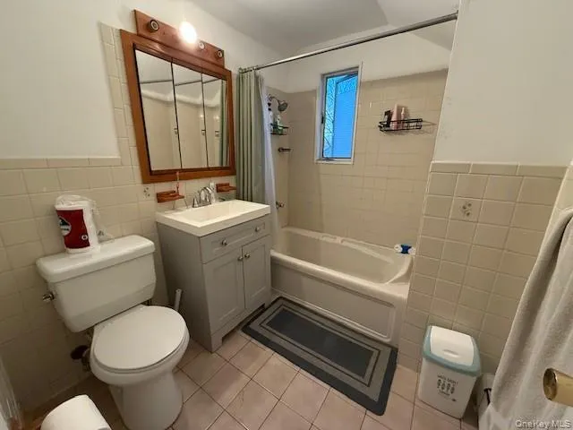 Full bathroom featuring tile walls, vanity, shower / tub combo with curtain, light tile patterned floors, and wainscoting Full bathroom featuring tile walls, vanity, shower / tub combo with curtain, light tile patterned floors, and wainscoting
