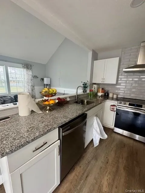 Kitchen featuring stainless steel appliances, white cabinetry, dark stone countertops, lofted ceiling, and wall chimney exhaust hood Kitchen featuring stainless steel appliances, white cabinetry, dark stone countertops, lofted ceiling, and wall chimney exhaust hood