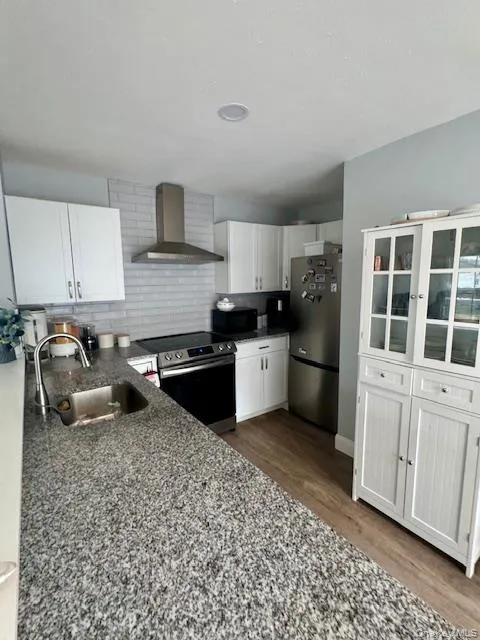Kitchen featuring white cabinetry, dark stone counters, wall chimney exhaust hood, stainless steel appliances, and backsplash Kitchen featuring white cabinetry, dark stone counters, wall chimney exhaust hood, stainless steel appliances, and backsplash