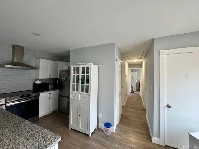 Kitchen featuring wall chimney exhaust hood, black appliances, white cabinets, dark wood-type flooring, and tasteful backsplash Kitchen featuring wall chimney exhaust hood, black appliances, white cabinets, dark wood-type flooring, and tasteful backsplash