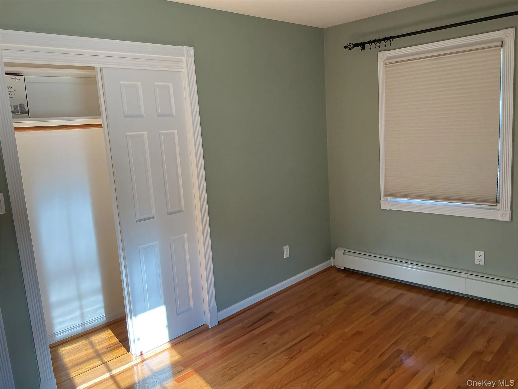 Unfurnished bedroom featuring wood finished floors, a closet, and a baseboard radiator Unfurnished bedroom featuring wood finished floors, a closet, and a baseboard radiator