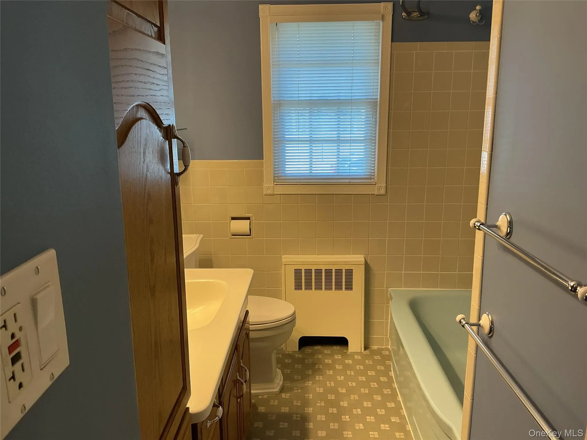 Full bath with vanity, radiator heating unit, tile walls, wainscoting, and shower combination Full bath with vanity, radiator heating unit, tile walls, wainscoting, and shower combination