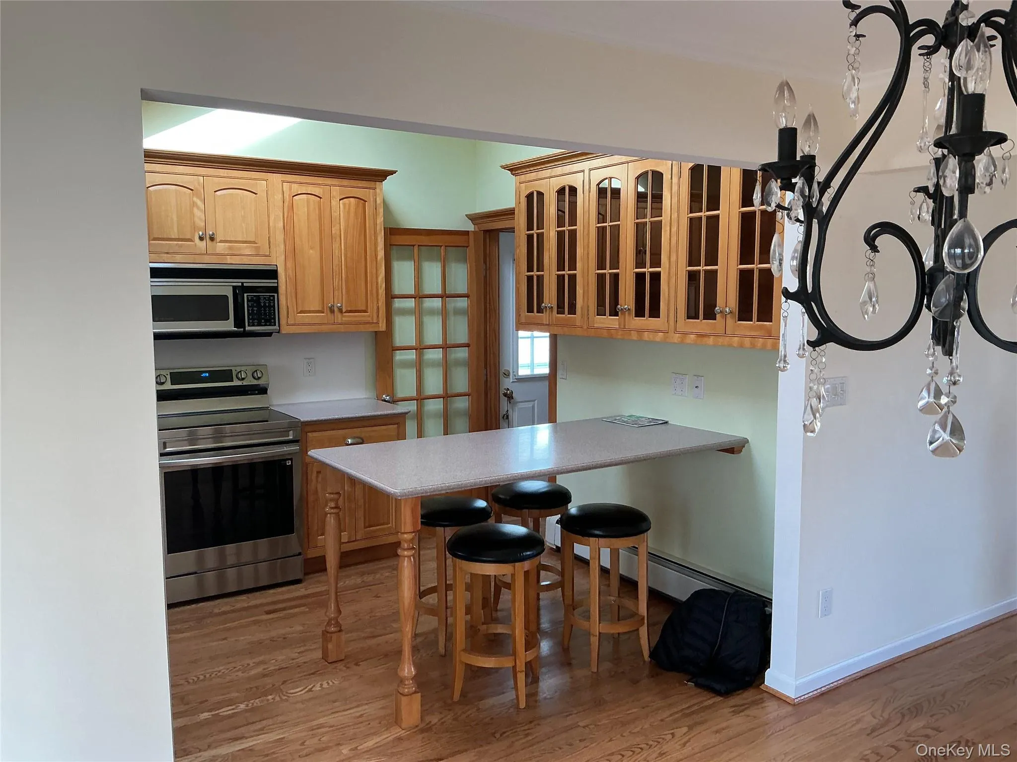 Kitchen with glass insert cabinets, appliances with stainless steel finishes, a kitchen bar, light countertops, and light wood-type flooring Kitchen with glass insert cabinets, appliances with stainless steel finishes, a kitchen bar, light countertops, and light wood-type flooring