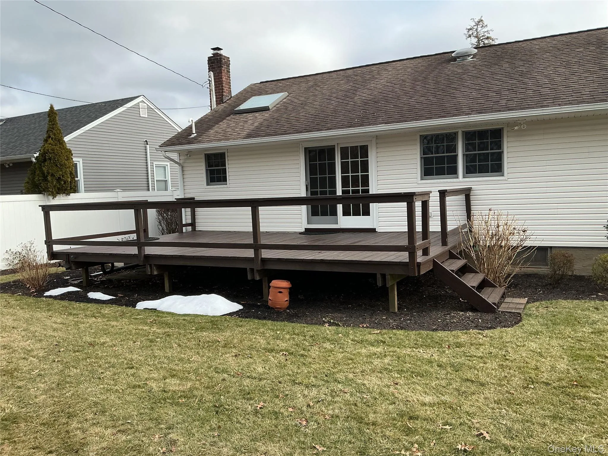 Rear view of house featuring a deck, a yard, a chimney, and roof with shingles Rear view of house featuring a deck, a yard, a chimney, and roof with shingles